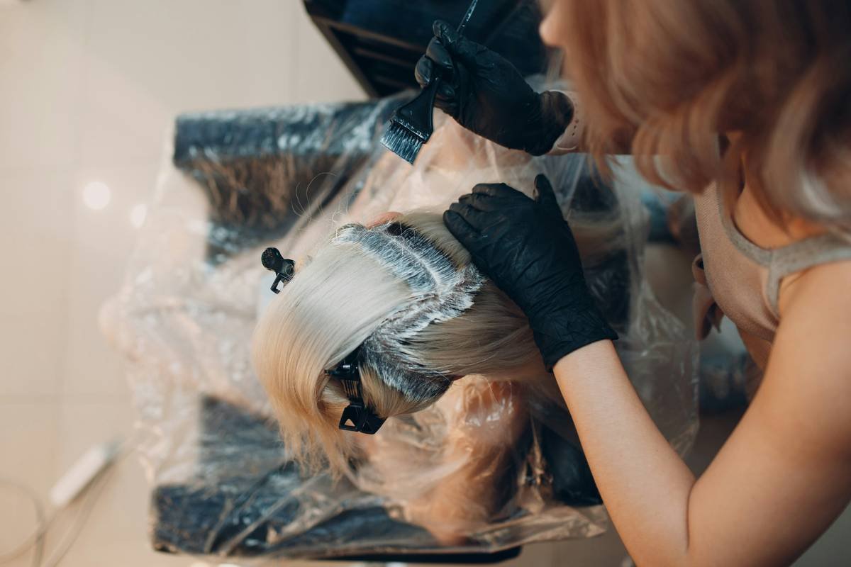 Young woman hairdresser dying hair at beauty salon. Professional hair roots coloring