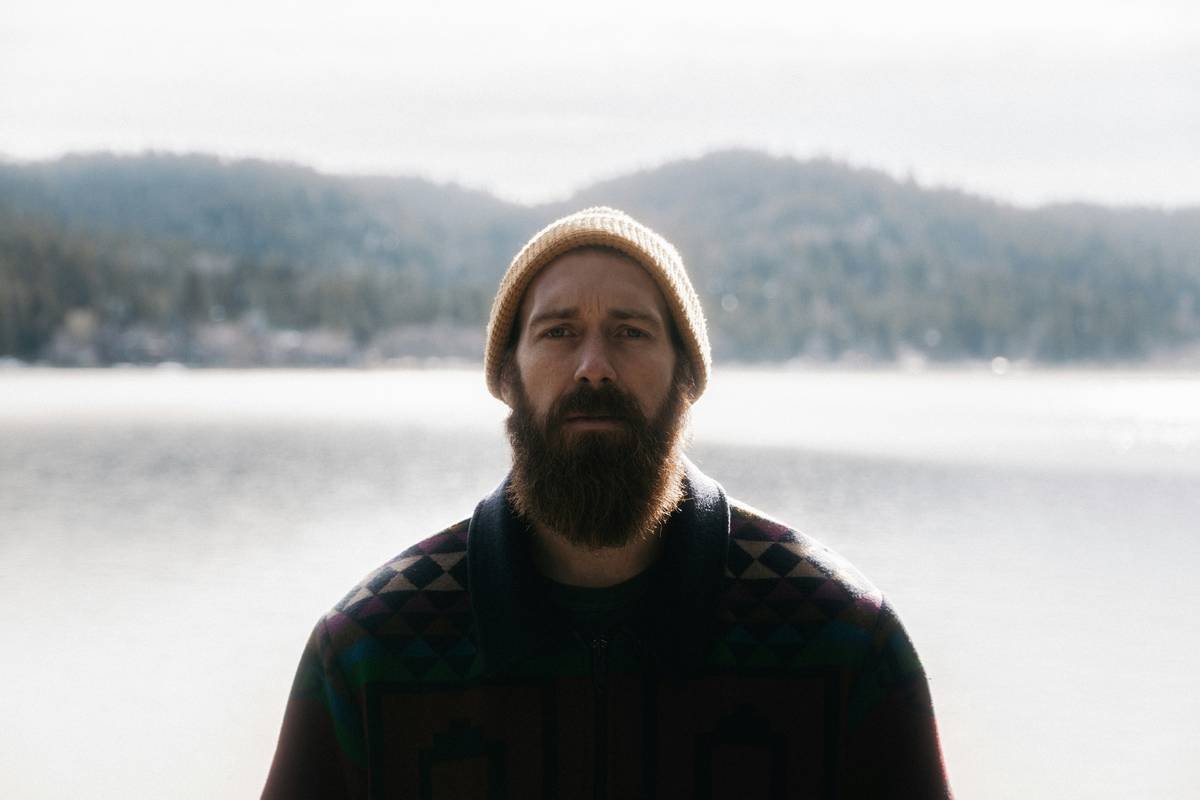 a man with a beard standing in front of a lake