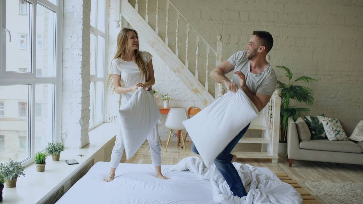 Young happy and loving couple having pillow fight in the bed at home